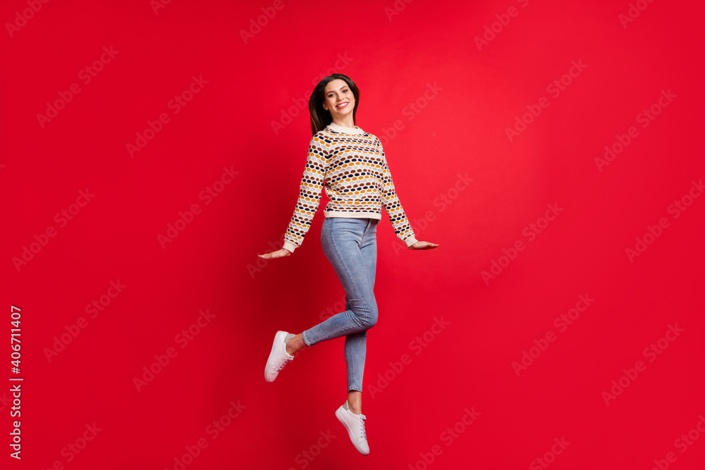 Full length body size photo of nice pretty girl jumping wearing stylish outfit jeans sweater isolated vivid red color background Full length body size photo of nice pretty girl jumping wearing stylish outfit jeans sweater isolated vivid red color background