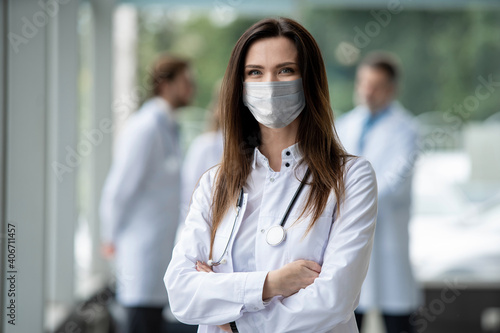 Portrait of young female doctor in medical mask looking at camera in the consultation