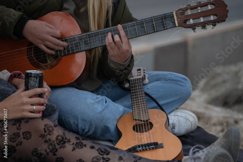 Blonde girl sitting on the rocks by the sea playing guitar and singing in Palma de Mallorca, Spain