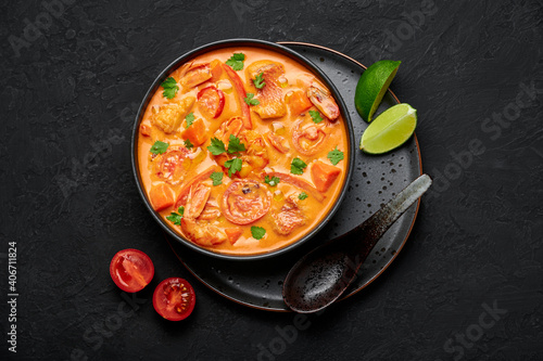 Moqueca with Fish and Shrimps in black bowl on dark slate table top. Brazilian sea food curry dish with coconut milk and vegetables. Top view