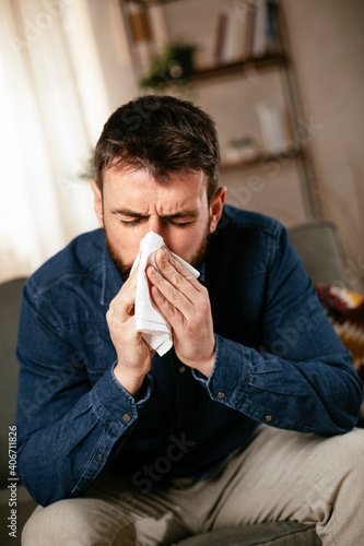 Sick man at home. Young man sitting on sofa having fever..