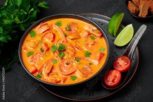 Moqueca with Fish and Shrimps in black bowl on dark slate table top. Brazilian sea food curry dish with coconut milk and vegetables. photo