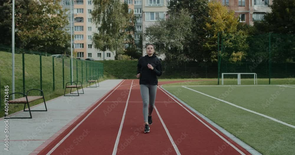 Attractive millennial woman looking ahead and breathing deeply while jogging. Pretty female person in training suit running at sports field. Concept of healthy lifestyle, motivation. Attractive millennial woman looking ahead and breathing deeply while jogging. Pretty female person in training suit running at sports field. Concept of healthy lifestyle, motivation.