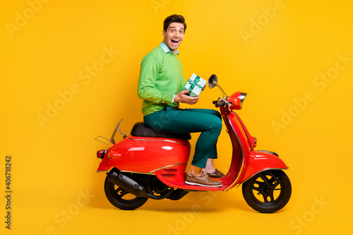 Full size profile photo of impressed funny guy sit in moped hold small giftbox isolated on yellow color background © deagreez