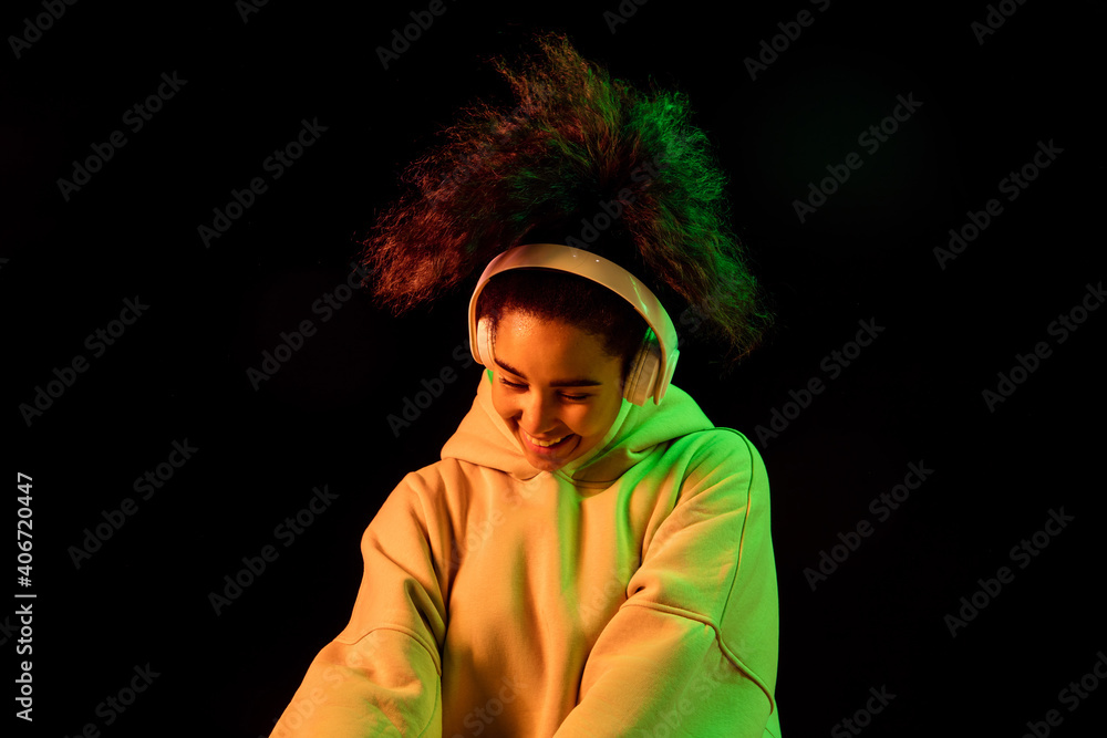 Youth. African-american woman's portrait on dark background in orange-green neon light. Listening to music with headphones. Concept of human emotions, facial expression, sales, ad, fashion. Copyspace. Youth. African-american woman's portrait on dark background in orange-green neon light. Listening to music with headphones. Concept of human emotions, facial expression, sales, ad, fashion. Copyspace.