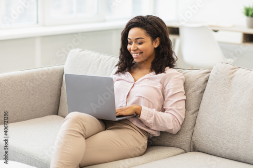 Black woman sitting on couch and working on laptop © Prostock-studio