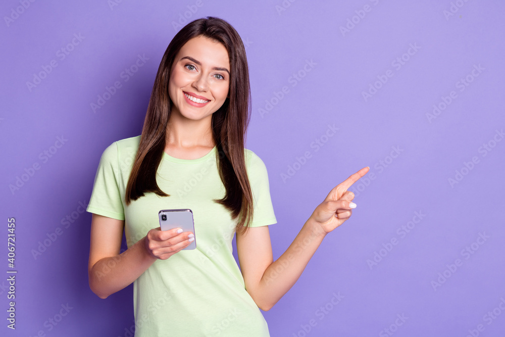 Photo portrait of happy girl holding smartphone pointing showing with finger at copyspace smiling isolated on bright purple color background Photo portrait of happy girl holding smartphone pointing showing with finger at copyspace smiling isolated on bright purple color background