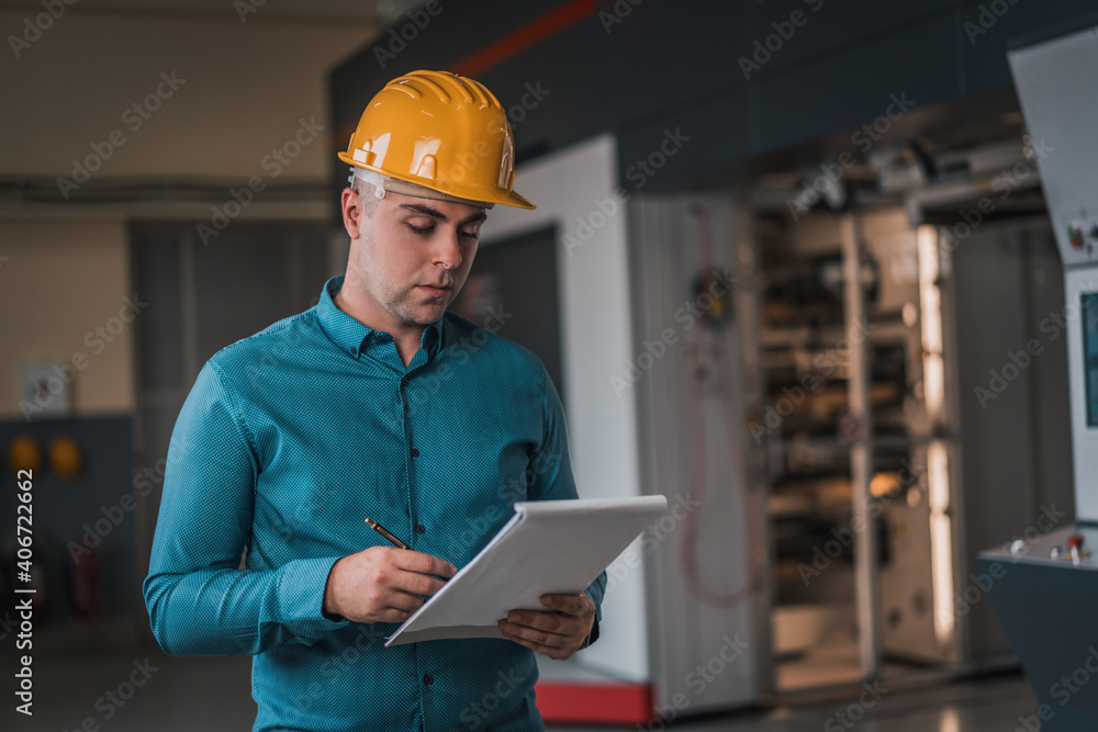 Engineer supervisor in a factory with hamlet. Mechanical technician operative next to industrial machine. Engineer in the factory. Interior of production department. Engineer supervisor in a factory with hamlet. Mechanical technician operative next to industrial machine. Engineer in the factory. Interior of production department.