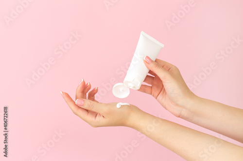Female hands apply cosmetic skin care moisturizer cream on pink background