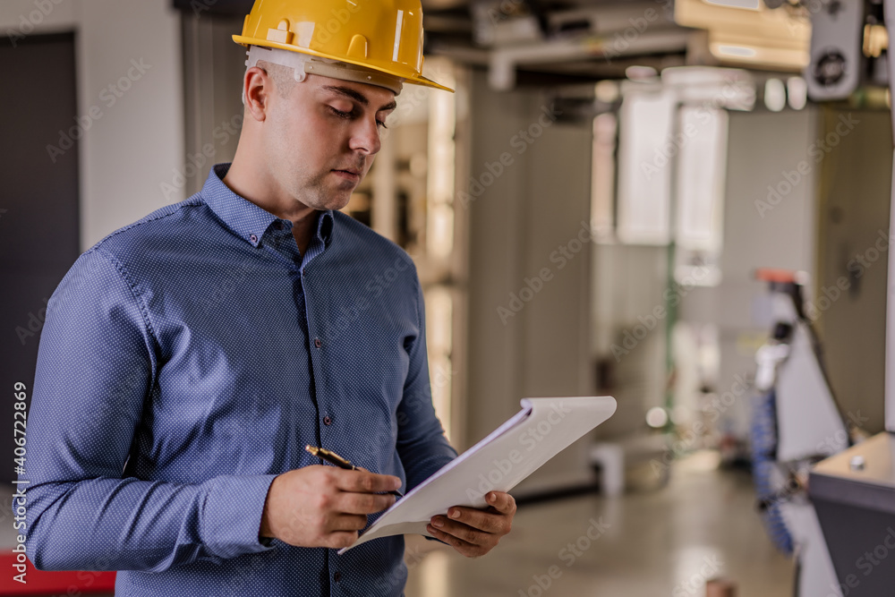 Engineer supervisor in a factory with hamlet. Mechanical technician operative next to industrial machine. Engineer in the factory. Interior of production department. Engineer supervisor in a factory with hamlet. Mechanical technician operative next to industrial machine. Engineer in the factory. Interior of production department.