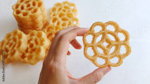 A hand holding a honeycomb cookie, with some more in the background. It is also known as kuih loyang in Malaysia, and is a popular deep-fried sweet snack during festivals.  photo