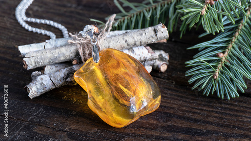 Amazing glittering bright yellow Baltic amber pendant lies on the birch branches with fir twigs on the wooden surface.  Amber texture,  ancient good luck charm. 
