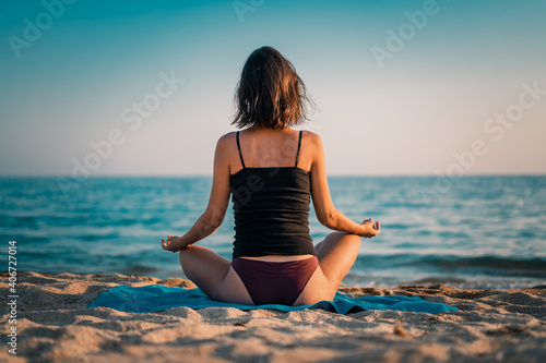 Young beautiful woman practicing pose from yoga on the beach at sunset. Female on beach exercising on vacation