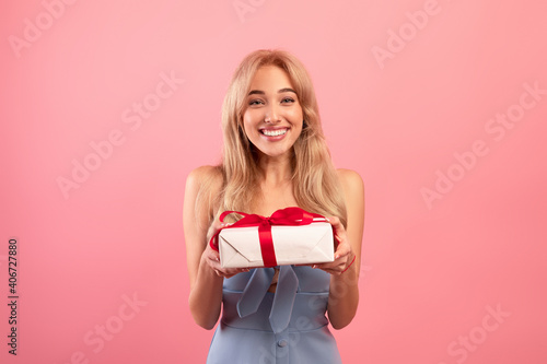 Charming millennial lady holding gift box with ribbon, receiving Woman's Day or birthday surprise on pink background
