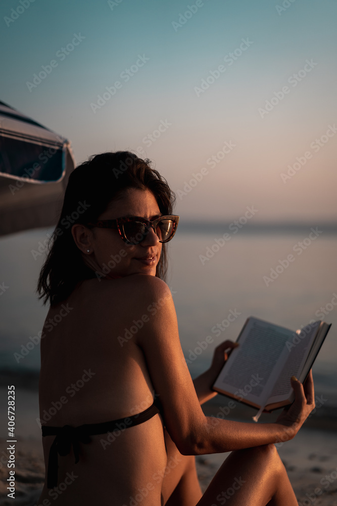 Young beautiful woman sitting on beach reading a book