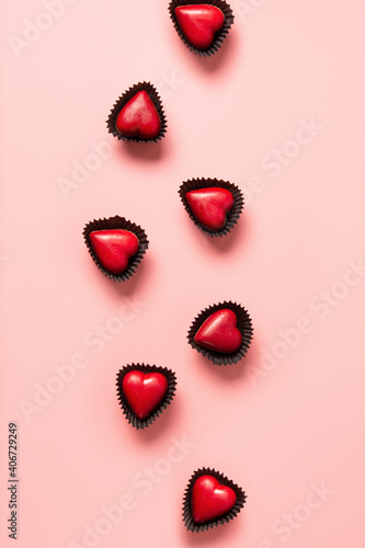 Red chocolate sweets as hearts on pink background. Valentine's day romantic tasty treats. Vertical greeting card.