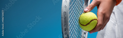 cropped view of sportive young woman holding tennis racket and ball while playing on blue, banner