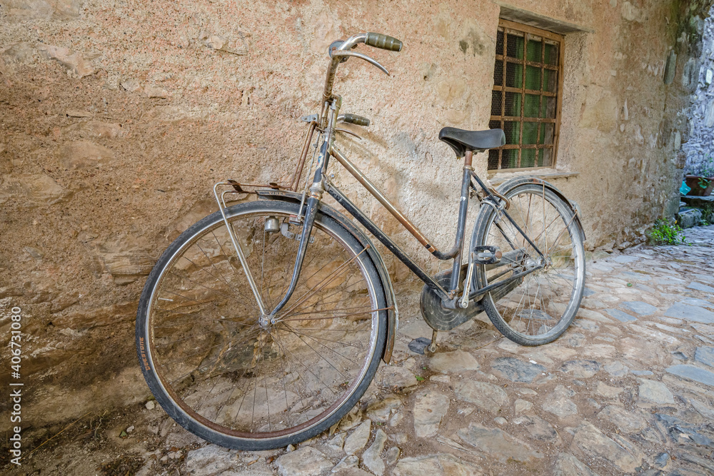 View of forgotten old bike parked against the wall in one of the empty stone streets of an abandoned mountain village View of forgotten old bike parked against the wall in one of the empty stone streets of an abandoned mountain village