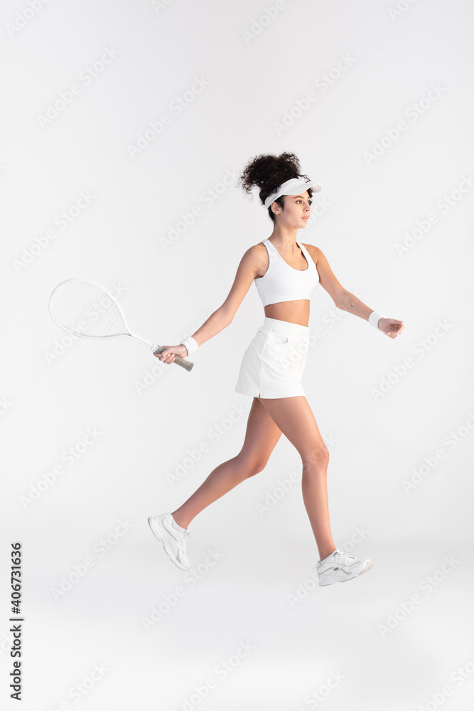 full length of curly young player in sportswear holding racket and playing tennis on white full length of curly young player in sportswear holding racket and playing tennis on white