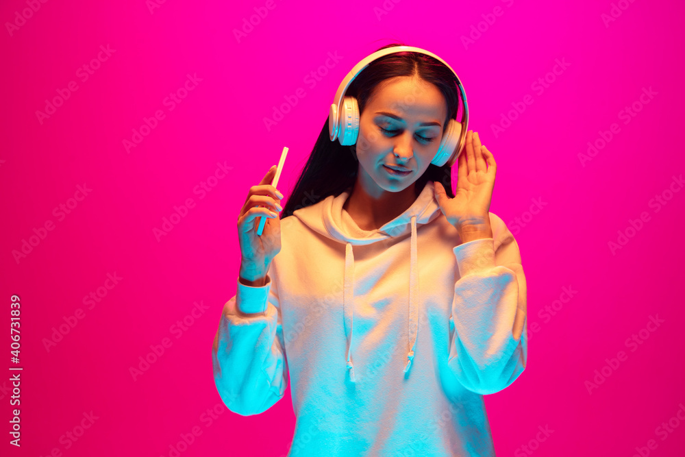 Dancing. Caucasian woman's portrait isolated on pink studio background in mixed neon light. Listening to music. Concept of human emotions, facial expression, sales, ad, fashion. Copyspace.