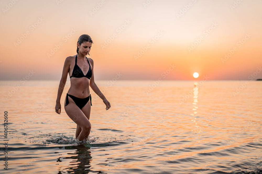 Fototapeta premium Young beautiful woman having fun in water at beach. Summer photo of young beautiful girl in sea swimming and having fun. Female on beach enjoying sea vacation traveling
