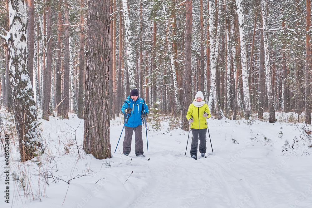 Mature couple in winter sportswear are skiing in snowy forest.