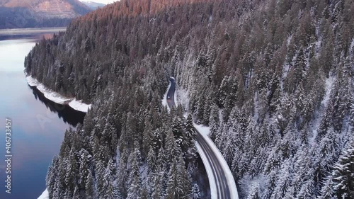 Aerial cinematic view of car drive on a forest road in winter with snow on top photo