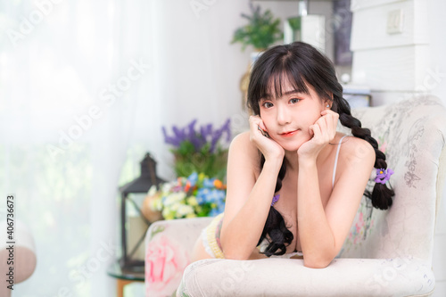 A cute, long-haired Asian Thai woman wearing yellow lingerie and lying down with her chin on the sofa in the living room.