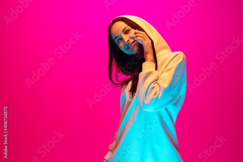 Talking phone. Caucasian woman's portrait isolated on pink studio background in mixed neon light. Listening to music. Concept of human emotions, facial expression, sales, ad, fashion. Copyspace.