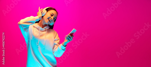 Dancing. Caucasian woman s portrait isolated on pink studio background in mixed neon light. Listening to music. Concept of human emotions  facial expression  sales  ad  fashion. Copyspace. Flyer