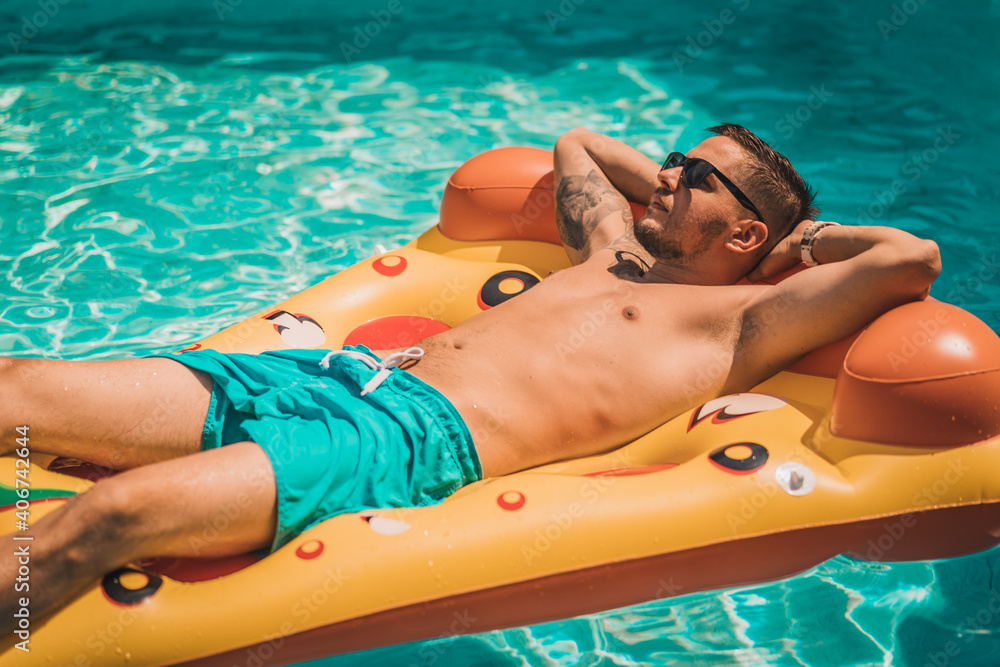 Handsome young man enjoying summer time in pool on the inflatable mattress in the swimming pool having fun.