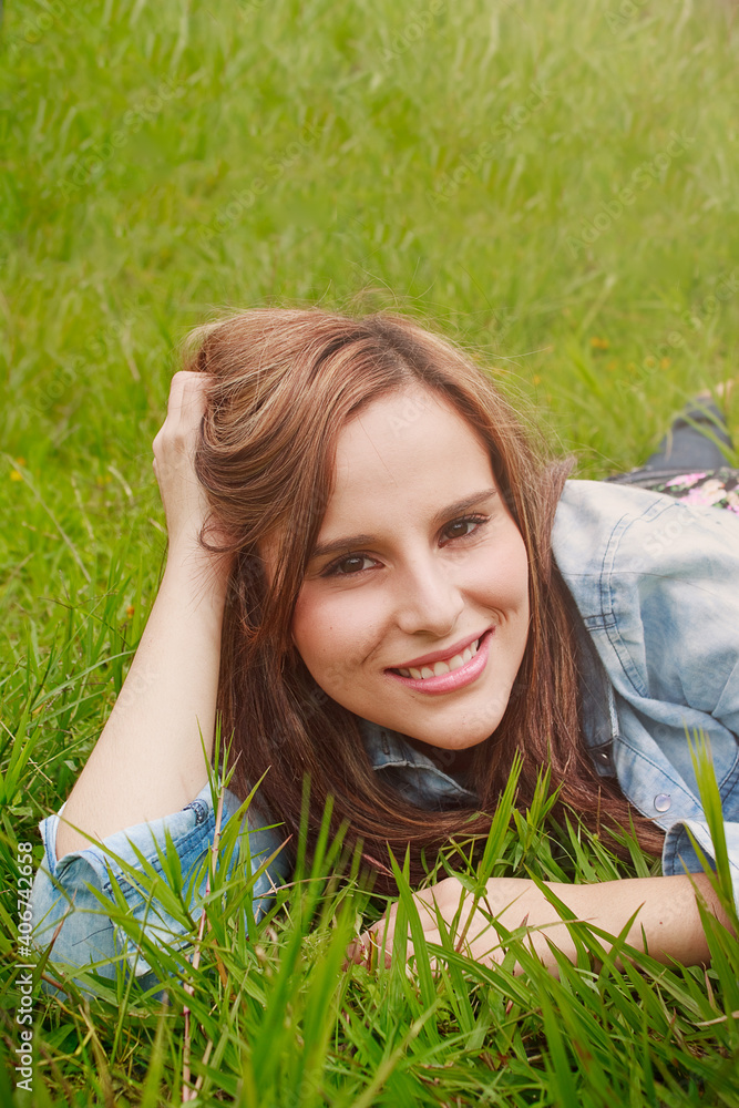 Young woman lying in the grass while looking at the camera Young woman lying in the grass while looking at the camera