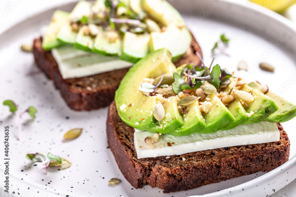 Healthy avocado toasts with rye bread, sliced avocado, cheese, pumpkin, nut and sesame for breakfast or lunch. Vegetarian food. Vegan menu. Food recipe background. Close up Healthy avocado toasts with rye bread, sliced avocado, cheese, pumpkin, nut and sesame for breakfast or lunch. Vegetarian food. Vegan menu. Food recipe background. Close up