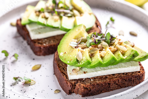 Healthy avocado toasts with rye bread, sliced avocado, cheese, pumpkin, nut and sesame for breakfast or lunch. Vegetarian food. Vegan menu. Food recipe background. Close up
