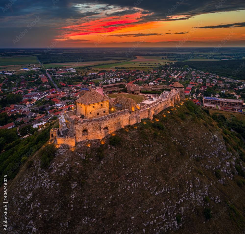 Sumeg, Hungary - Aerial view of the famous illuminated High Castle of Sumeg in Veszprem county at sunset with colorful clouds and dramatic colors of sunset at background on a summer afternoon