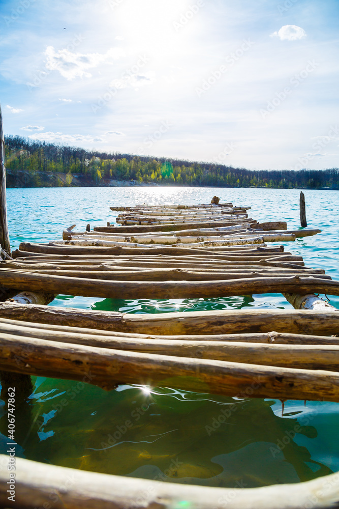Fototapeta premium Wooden masonry stands on the water isolated. Entry into the lake from a wooden bridge into the lake
