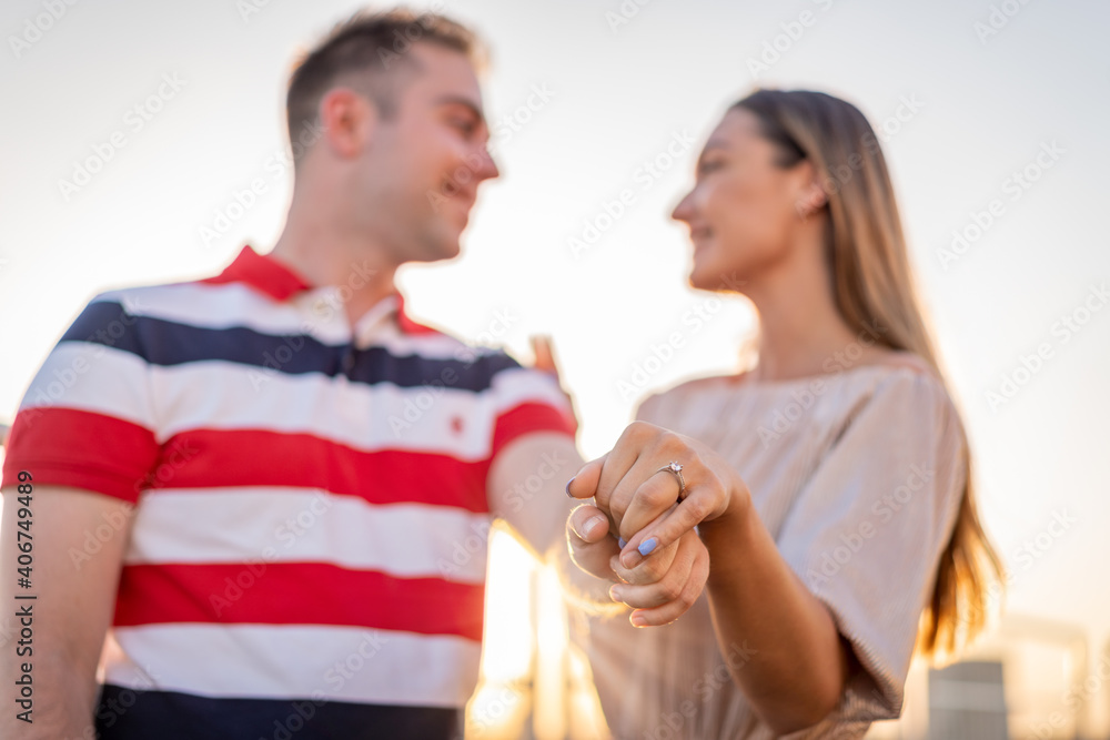 Naklejka premium Beautiful couple engaging on rooftop. Man on his knee asking his girlfriend to merry him. Love and beauty. Engagement on roof top with beautiful view