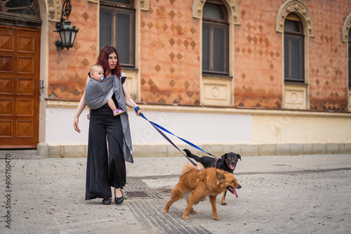 A young woman with a baby in a sling walking her dogs in city