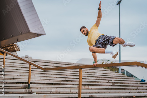 Man doing sports and training outdoors in city. Man jumping over the fence and working out hard. Parkour elements in workout. 