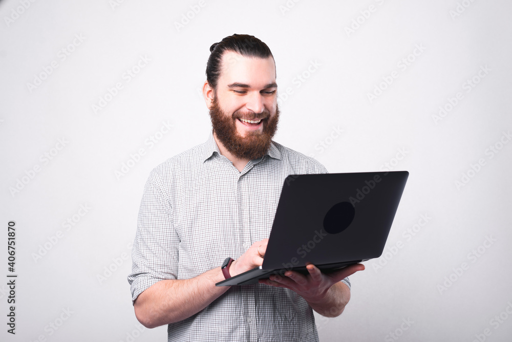 Portrait of happy bearded man in shirt using laptop over white wall. Portrait of happy bearded man in shirt using laptop over white wall.