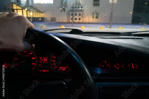 Driver's hand on the steering wheel of the car with a red illuminated dashboard, photo from the inside in motion