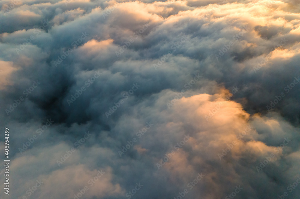 Aerial view over surface of white dense clouds at sunset.
