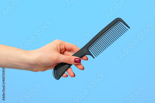Bild auf Leinwand Female hand holding hair comb against blue background