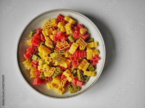 Colorful pasta in different shapes in light gray plate on a light gray background, closeup, horizontal