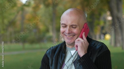 Smiling bald senior man talks on smartphone photo