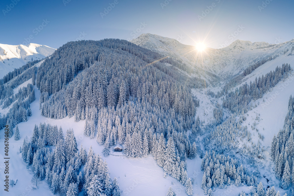 lonely single hut in forest clearing in snowy austrian mountains in winter with sunbeams on mountain ridge