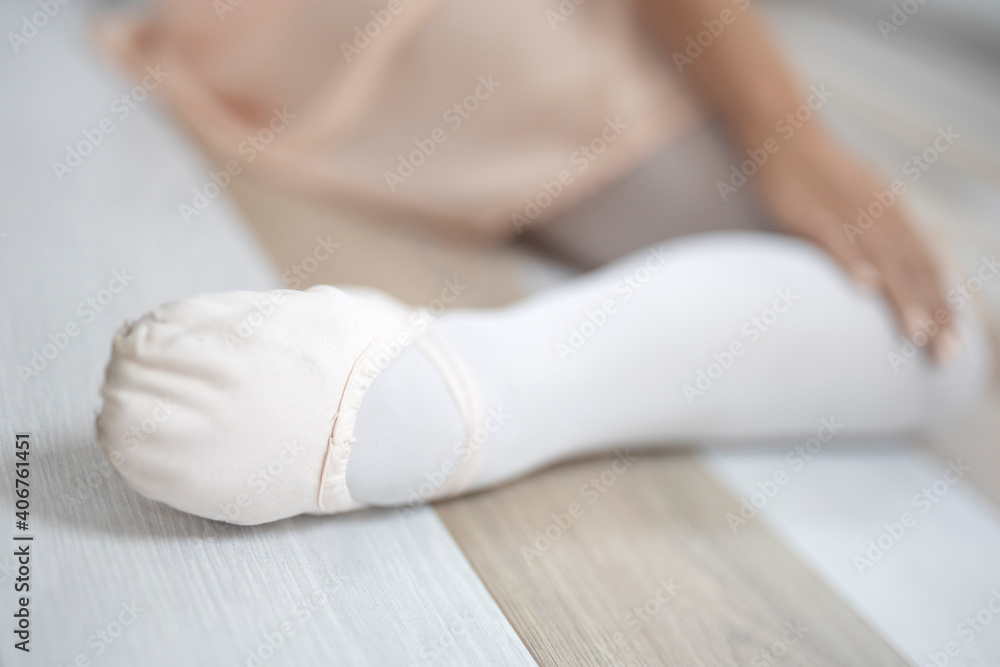 Close up view of ballerina`s foot in beige pointe shoe at wooden floor in ballet studio