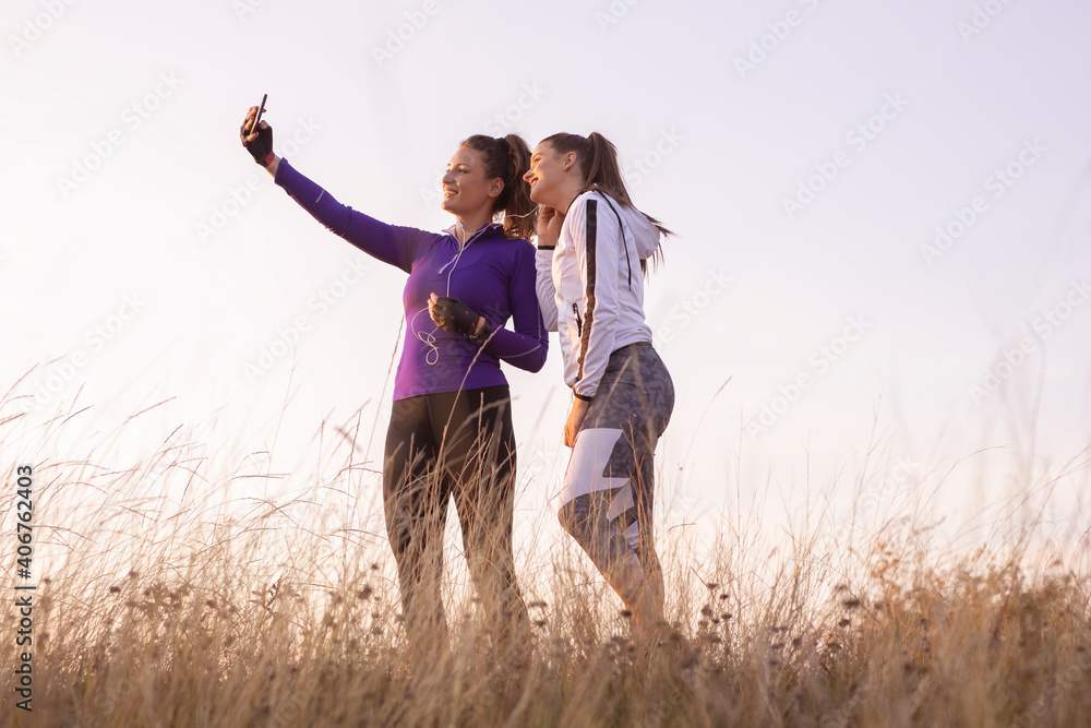 Young and happy best female friends in sportswear making selfie with smartphone together in nature after training Young and happy best female friends in sportswear making selfie with smartphone together in nature after training