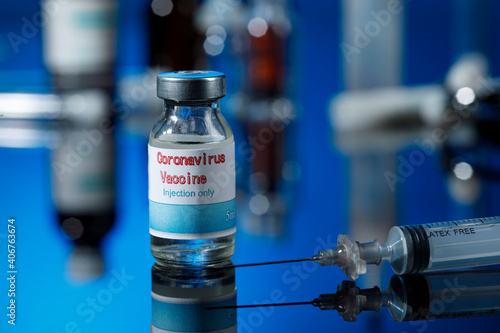 filetta di vetro del vaccino anti-covid con una siringa e posti sulla superfice riflettente del tavolo di un laboratorio, isolati su sfondo blu