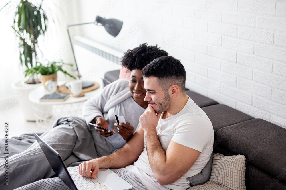 Multiethnic couple in bed in pijamas looking at notebook and enjoy in morning Multiethnic couple in bed in pijamas looking at notebook and enjoy in morning
